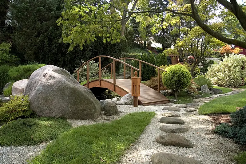 Harmonisch gestalteter Ziergarten mit Steinen, Brücke und Bepflanzung – Garten- und Landschaftsbau vom Profi
